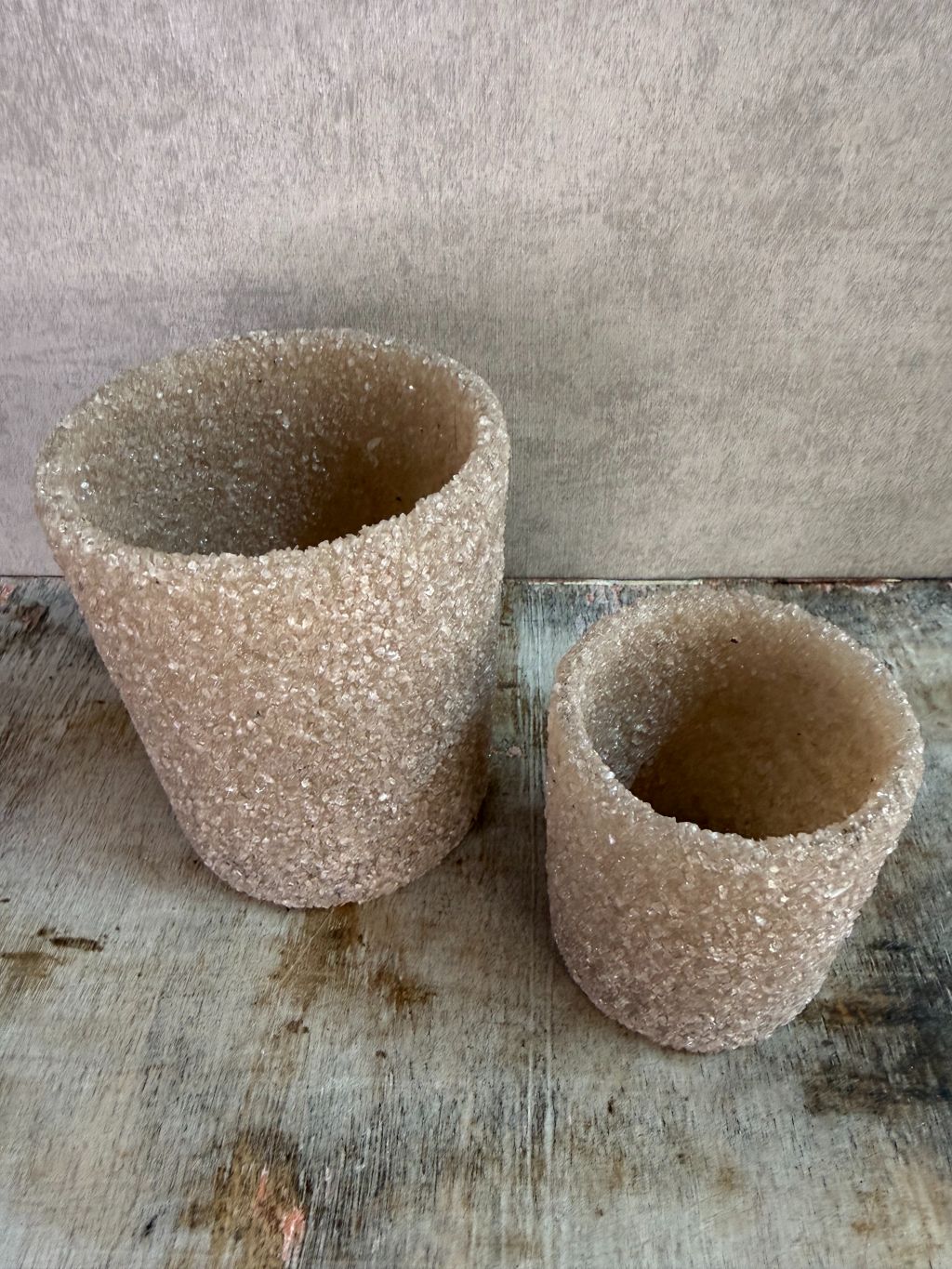 Set van twee zandkleurige waxinelichthouders met steentjesstructuur in verschillende formaten op een houten ondergrond.