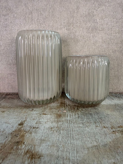 Twee beige waxinelichthouders van geribbeld glas in verschillende formaten op een houten ondergrond.