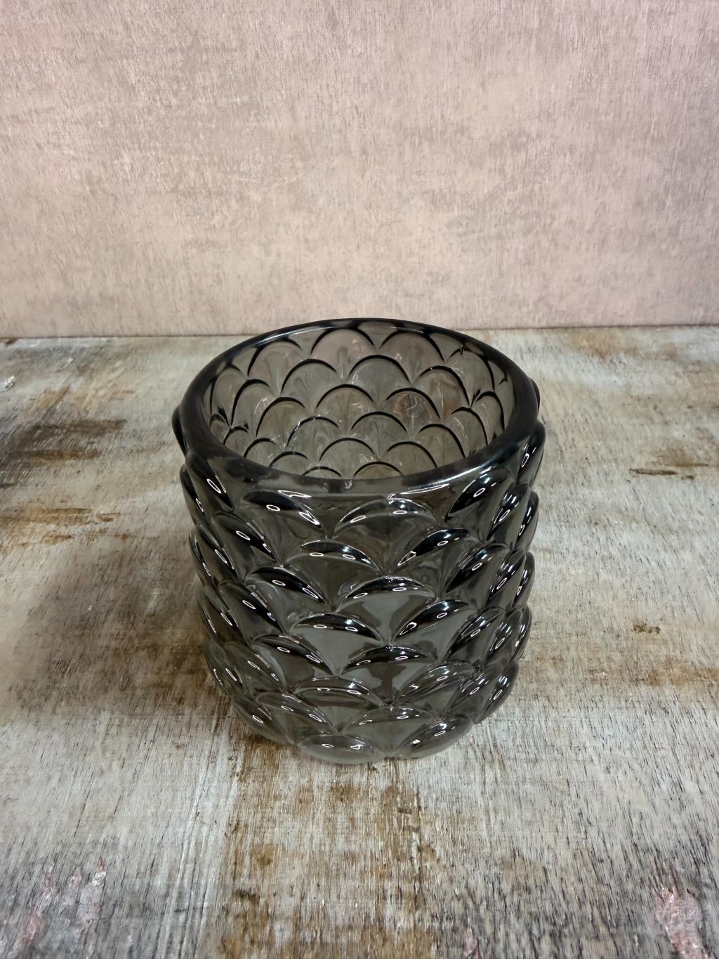 Transparant zwarte glazen waxinelichthouder Sculp met reliëfpatroon, geplaatst op een houten ondergrond.