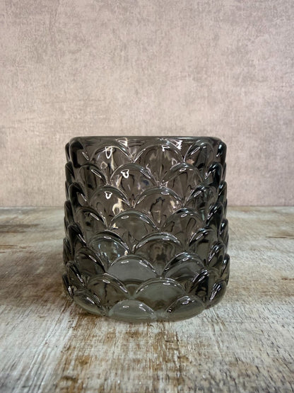 Transparant zwarte glazen waxinelichthouder Sculp met reliëfpatroon, geplaatst op een houten ondergrond.