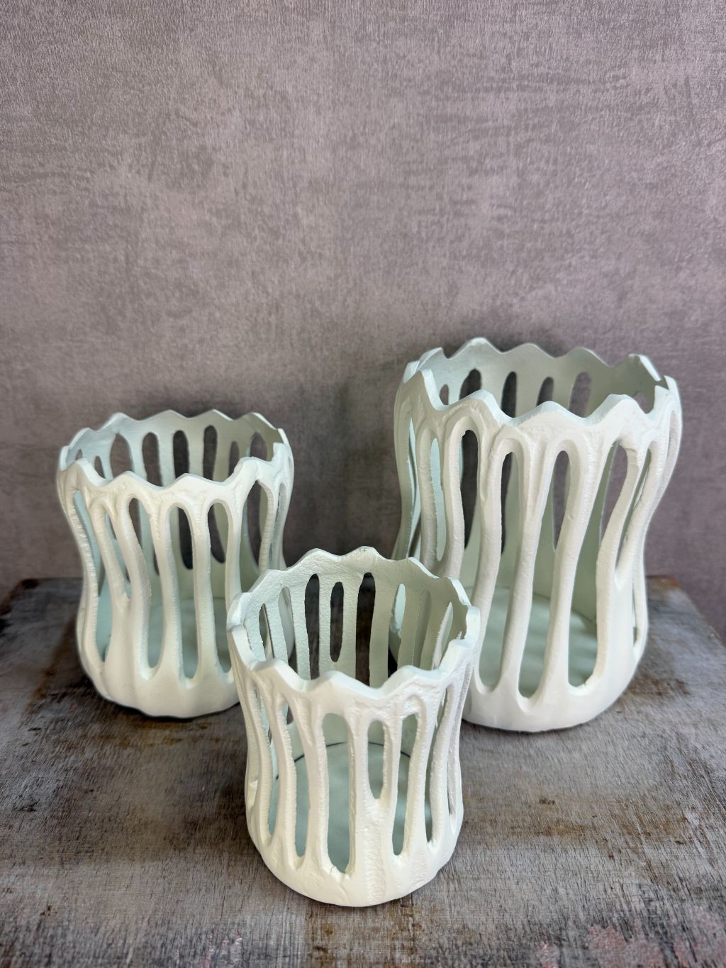 Drie crèmekleurige metalen waxinelichthouders Tivoli in verschillende formaten met open design op een houten ondergrond.