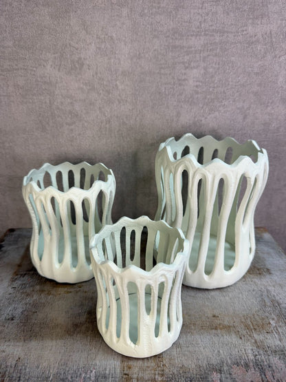 Drie crèmekleurige metalen waxinelichthouders Tivoli in verschillende formaten met open design op een houten ondergrond.