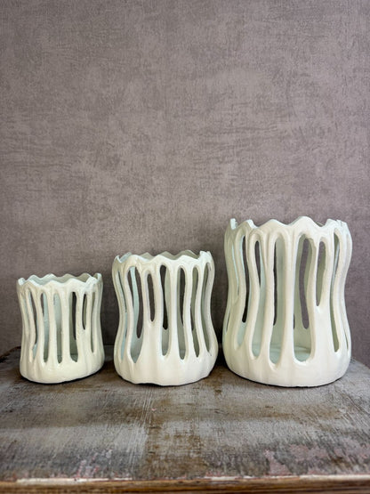 Drie crèmekleurige metalen waxinelichthouders Tivoli in verschillende formaten met open design op een houten ondergrond.