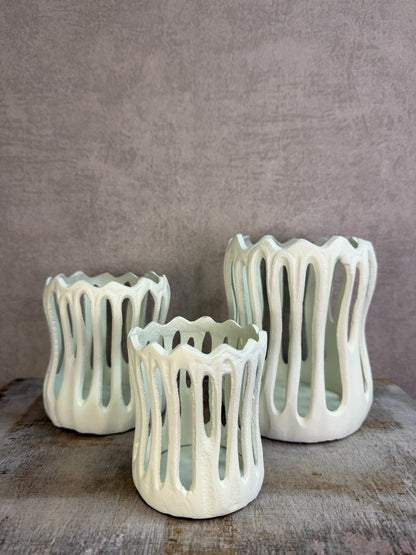 Drie crèmekleurige metalen waxinelichthouders Tivoli in verschillende formaten met open design op een houten ondergrond.