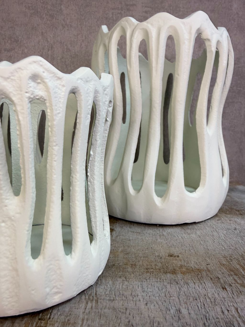 Drie crèmekleurige metalen waxinelichthouders Tivoli in verschillende formaten met open design op een houten ondergrond.