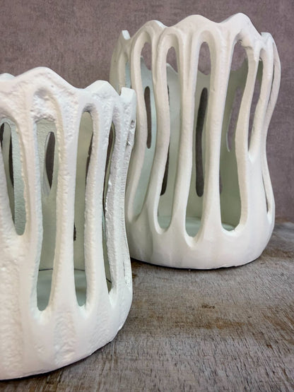 Drie crèmekleurige metalen waxinelichthouders Tivoli in verschillende formaten met open design op een houten ondergrond.