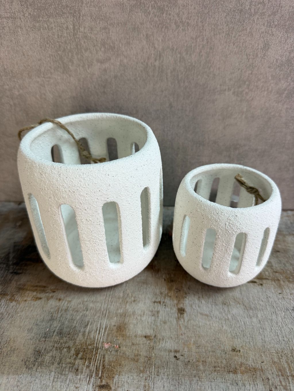 Twee witte keramieken waxinelichthouders Tobi in klein en groot formaat met opengewerkt patroon, geplaatst op een houten ondergrond.