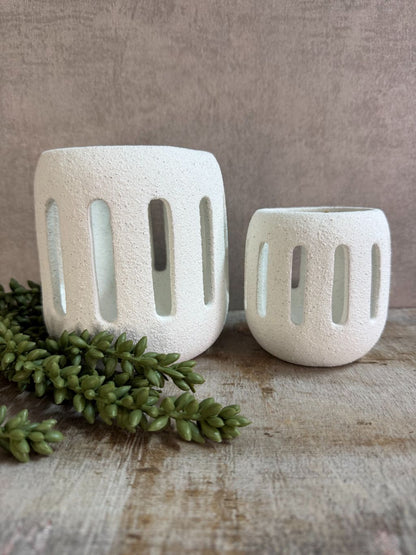 Twee witte keramieken waxinelichthouders Tobi in klein en groot formaat met opengewerkt patroon, geplaatst op een houten ondergrond. met erwtenplant