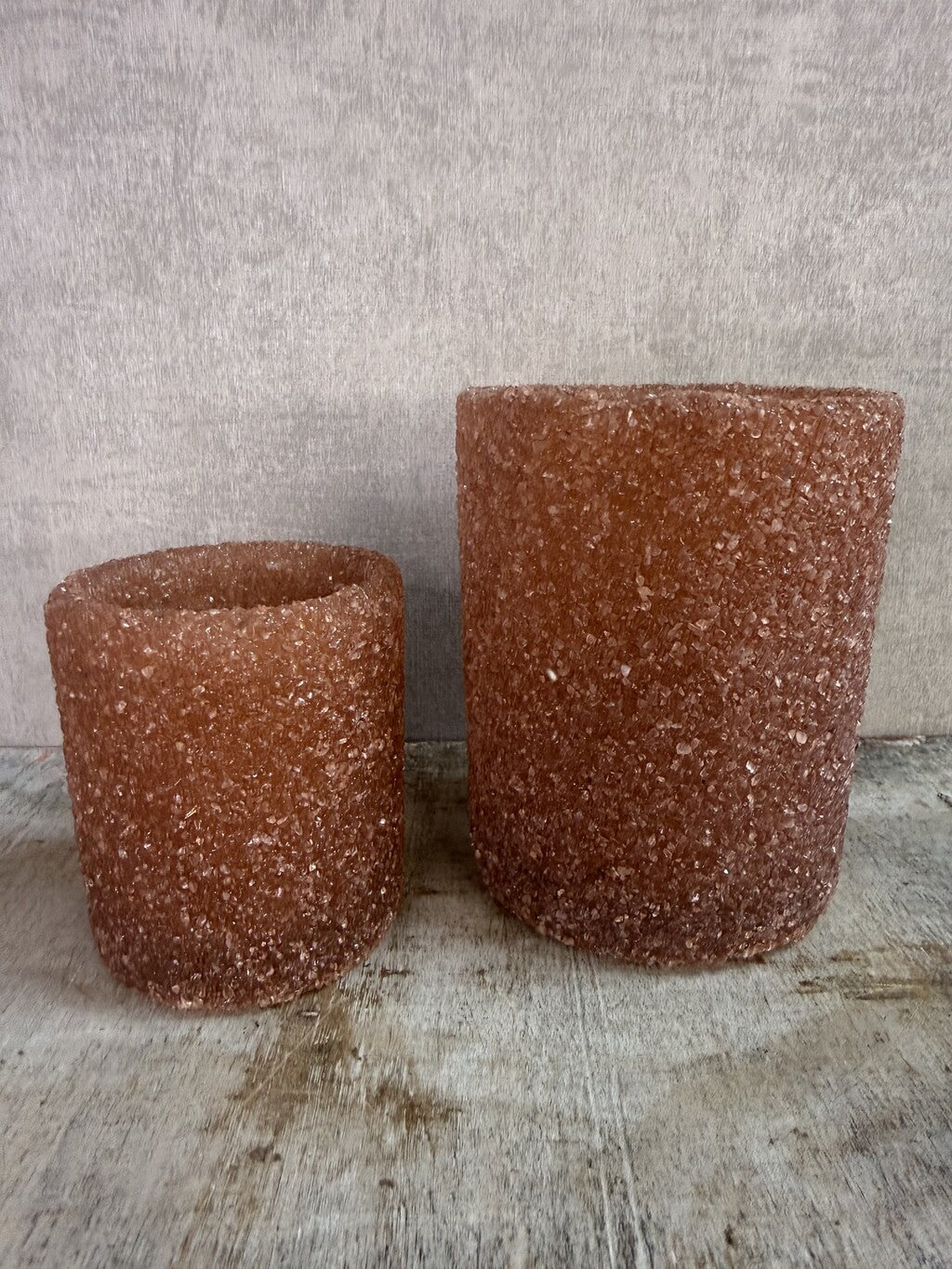 Bruine glazen waxinelichthouders met grove structuur in twee formaten op een houten ondergrond.