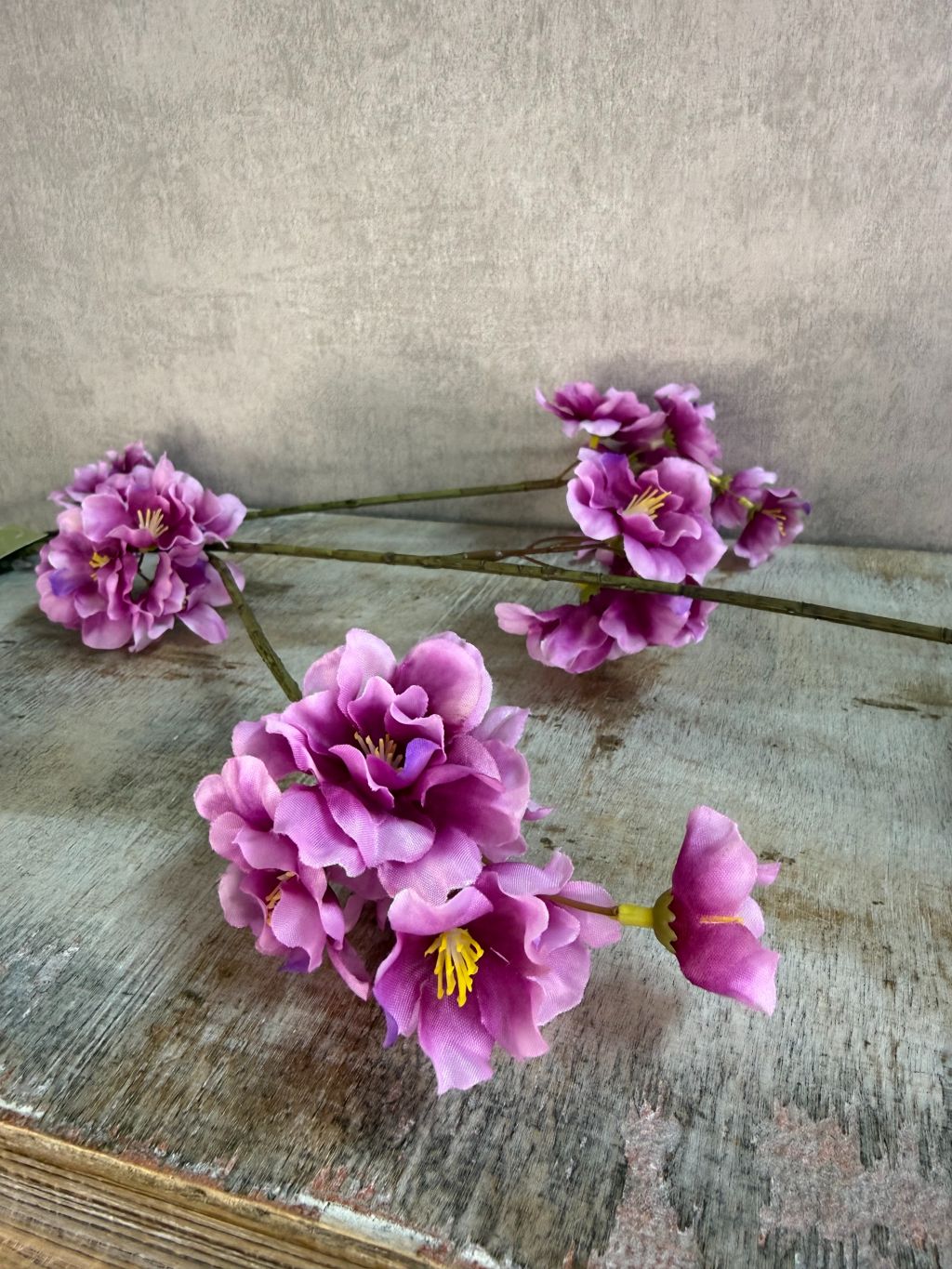 Zijden bloesemtak Prunus met paarse bloesems, slanke vertakking en een natuurlijke uitstraling tegen een neutrale achtergrond.