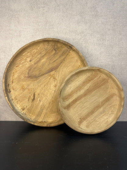 Twee ronde houten dienbladen in naturel kleur met zichtbaar nervenpatroon, staand tegen een neutrale wand op een zwart oppervlak.