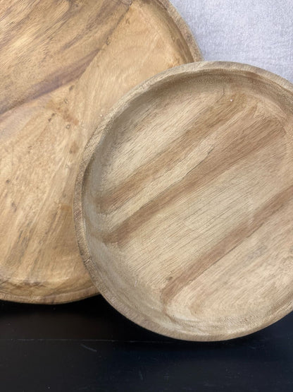 Twee ronde houten dienbladen in naturel kleur met zichtbaar nervenpatroon, staand tegen een neutrale wand op een zwart oppervlak.