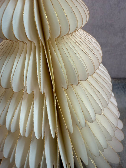 Crèmekleurige kerstboom van gevouwen papier met gouden glitteraccenten, staand op een houten ondergrond.