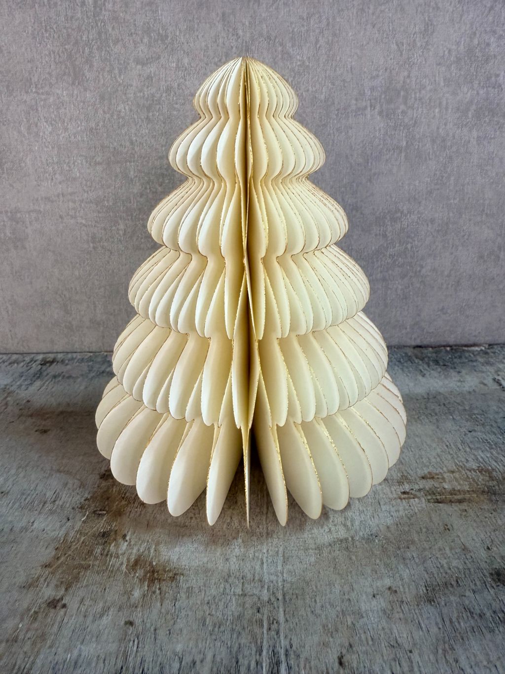 Crèmekleurige kerstboom van gevouwen papier met gouden glitteraccenten, staand op een houten ondergrond.