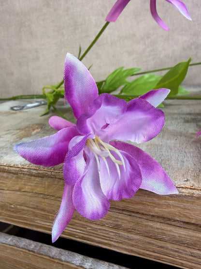 Paarse kunstbloem akelei met meerdere bloemen en groene bladeren tegen een neutrale achtergrond.