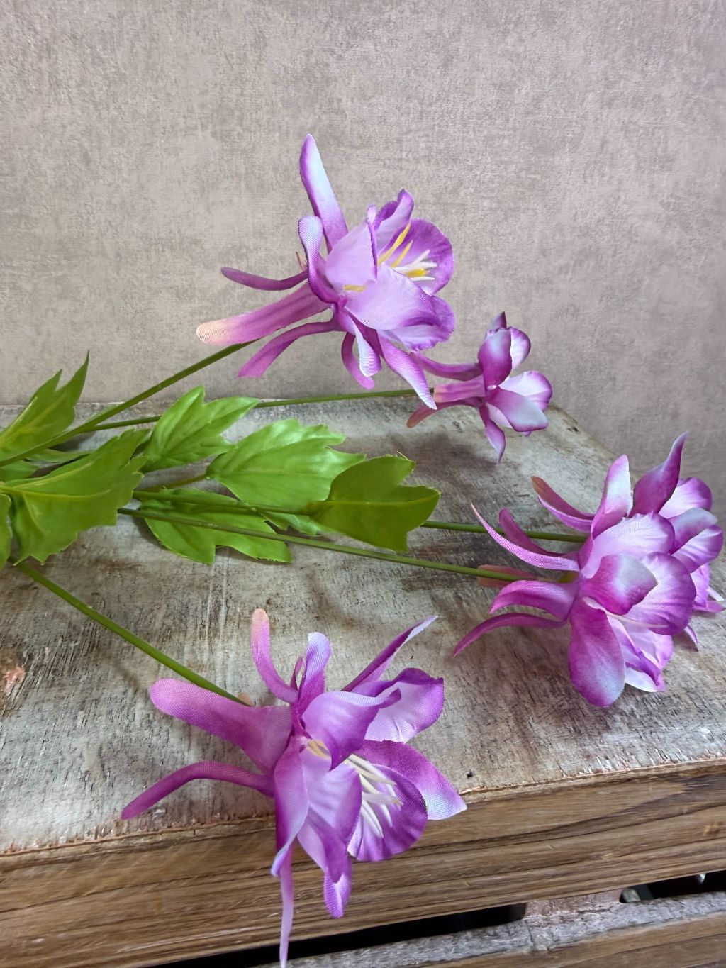 Paarse kunstbloem akelei met meerdere bloemen en groene bladeren tegen een neutrale achtergrond.