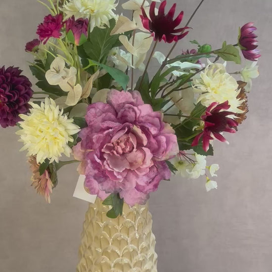 Video van Kunstboeket Noëlle – volle bos kunstbloemen in beige, bruin en bordeaux tinten in een beige vaas tegen grijze achtergrond.