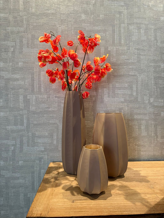 Tafel decoratie set met drie bruine vazen in verschillende hoogtes en een oranje kunsttak op een houten tafel tegen een lichte achtergrond.