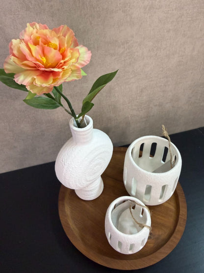 Tafel decoratie set met houten dienblad, witte vaas met bloem en twee witte waxinelichthouders tegen een neutrale achtergrond.